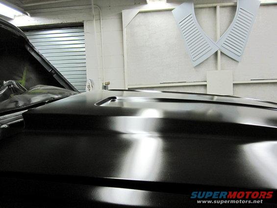 Black car hood with a raised scoop, showing reflections. Garage door in background