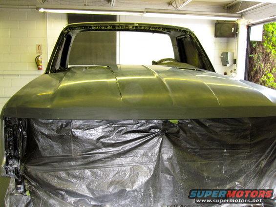 Unfinished Ford Bronco body, front view, covered in black plastic sheeting, showing the hood and windshield frame