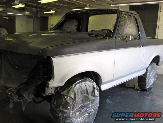 Ford Bronco in a garage, prepped for paint. Hood is dark gray, body is white primer