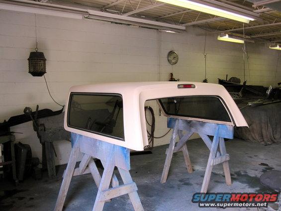 Cream-colored truck cap with tinted windows resting on blue sawhorses in a garage