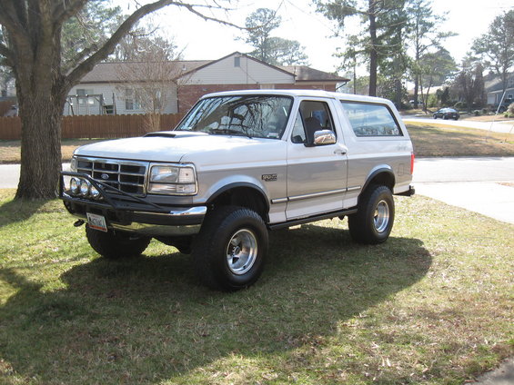 White and silver two-door Ford Bronco parked on a grassy lawn. It has a brush guard with lights on the front
