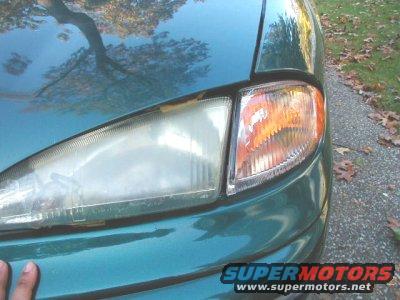 Close-up of a green car's front headlight assembly, showing a slightly fogged lens