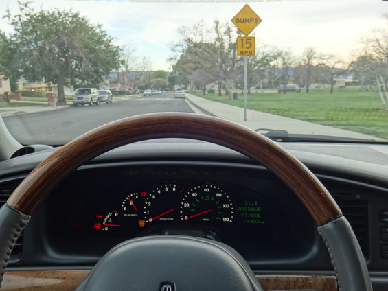 Dashboard of a 2000 Lincoln Continental with wood trim steering wheel, showing gauges and a street scene through the windshield
