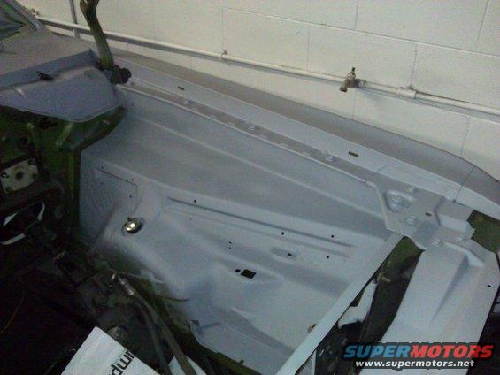 Car engine bay primed for restoration, showing inner fender and hood hinge area