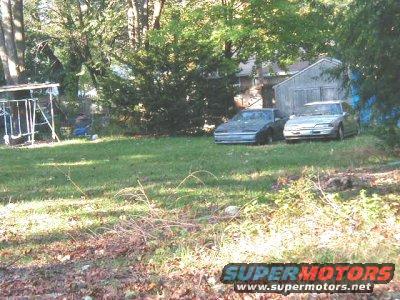 Two older cars parked in a grassy yard next to a shed. A swing set is visible to the left