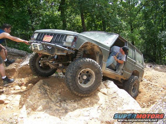 Green 1992 Jeep Cherokee navigating rocky terrain with a person assisting from outside