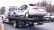 1989 Ford Bronco - A heavily damaged sedan is loaded onto a tow truck, with another vehicle visible in the background.