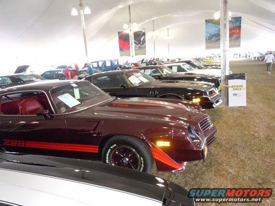 Maroon 1980s Chevrolet Camaro Z28 with red stripes, front 3/4 view, parked under a tent