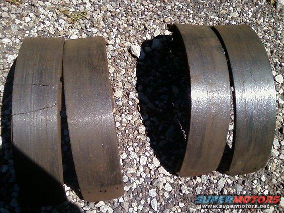 Two old, rusty brake drums sitting on gravel. One drum is cracked