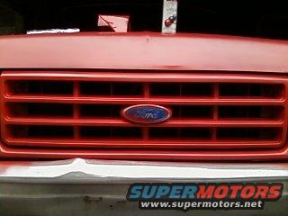 Red 1987 Ford F-150 grille with blue Ford oval emblem. White bumper visible below