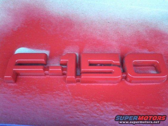 Red F-150 emblem on a red surface with white overspray