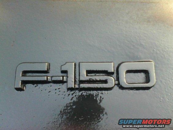Close-up of an F-150 badge on a metallic surface. Supermotors.net watermark in lower right
