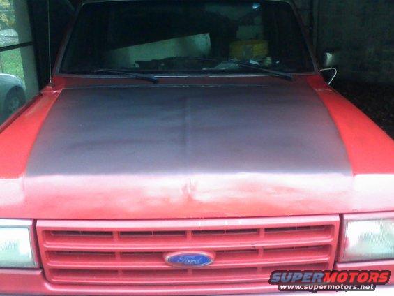 Front view of a red Ford truck with a dark hood and horizontal grille. Ford logo visible