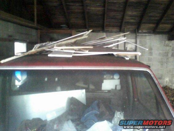 Red pickup truck parked inside a garage, its roof is covered with lumber and building materials