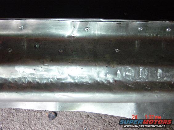 Close-up of a metal panel showing rivets and rough welds. Supermotors.net watermark in corner