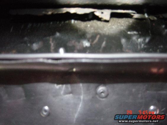Underside of a vehicle showing rust and metal components. A timestamp and website are visible