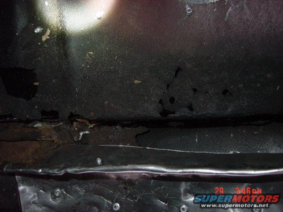 Close-up of a rusted metal frame and undercarriage of a vehicle. Some debris is visible