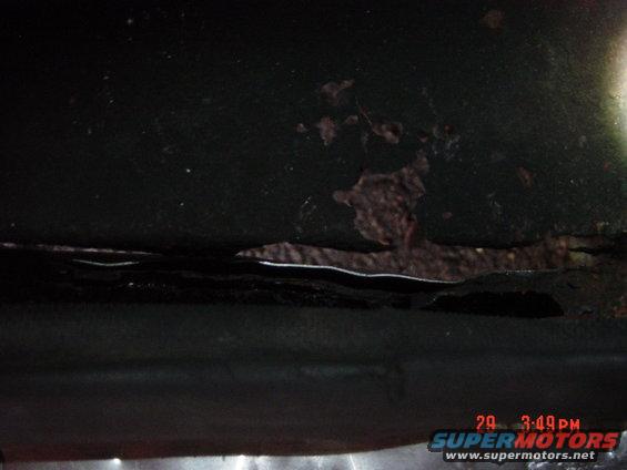 Close-up of rust and damage on a dark-colored vehicle panel