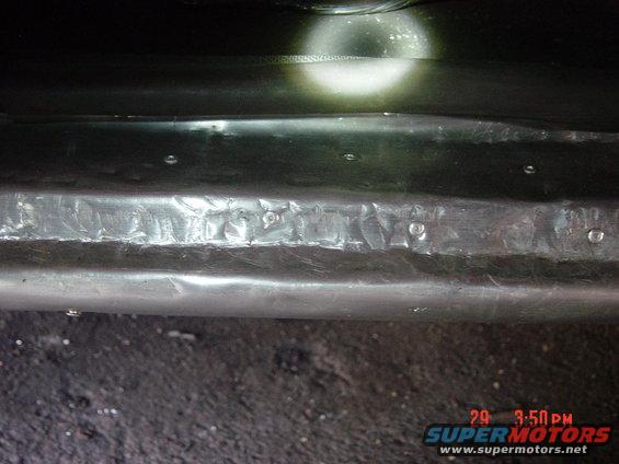 Damaged metal bumper with visible bolts and a bright light reflection