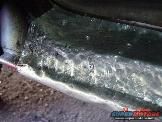 Close-up of a metal panel with visible welds and rivets, likely a repair on a truck's frame or body
