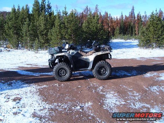 Camouflaged all-terrain vehicle parked on a dirt road with scattered snow, facing left