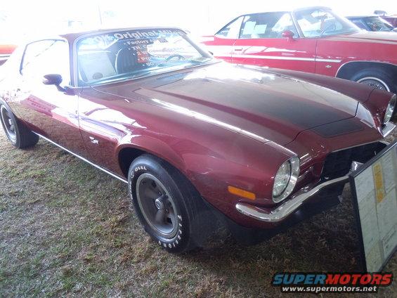 Maroon coupe with black hood stripe, 3/4 front view. Visible text on windshield