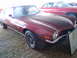 1982 Chevrolet Camaro - Maroon coupe with black hood stripe, 3/4 front view. Text visible on windshield. Another vehicle is parked behind.