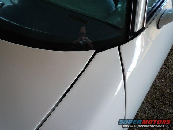 White car hood and windshield with a reflection of a person holding a camera. A watermark reads www.supermotors.net