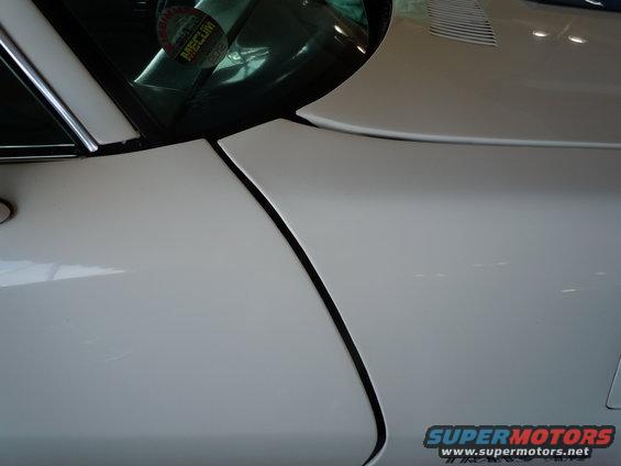 Close-up of a white car's body panel gap and a sticker on the windshield