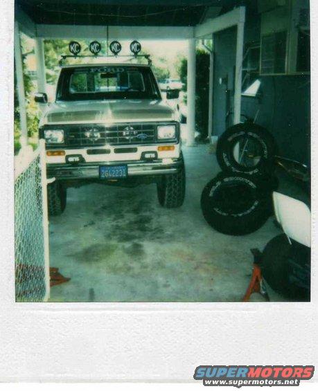 Front view of a gold Ford Ranger pickup truck with KC lights on the roof rack and a blue license plate
