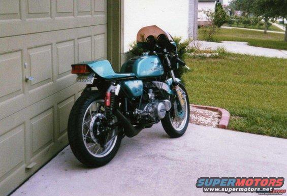 Teal motorcycle parked by garage, rear view