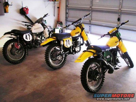 Three dirt bikes parked in a garage. One is white with number 47, two are yellow with numbers 14 and 400