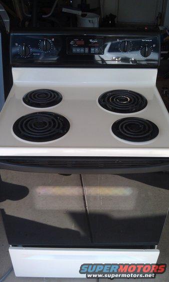 White electric stove with four burners and digital controls. A car is reflected in the oven door