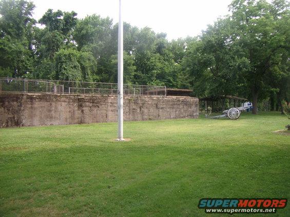 Historic cannon on wheels in a grassy field with trees and a concrete structure