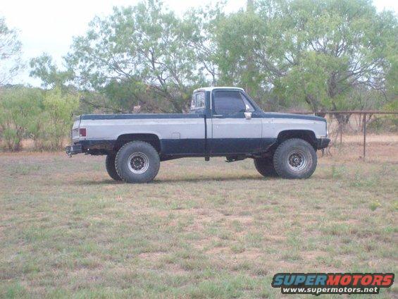 Two-tone pickup truck, silver and dark blue, lifted with large tires, parked on grass