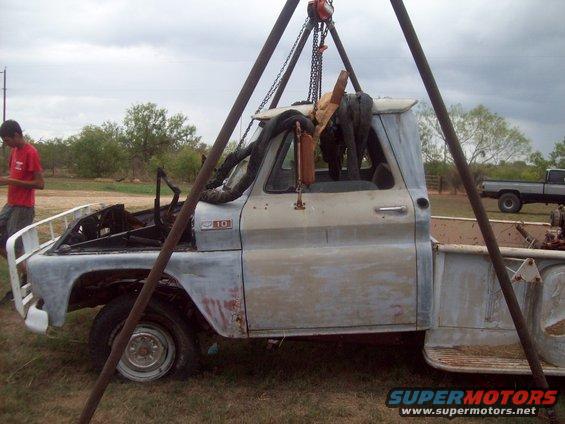 Side view of a light blue pickup truck with a "10" badge, being lifted by a crane