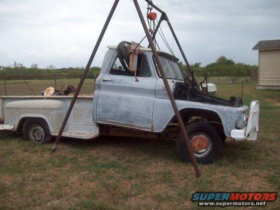 1960s pickup truck, primer gray, with engine hoist over the front end. Hood is open, showing engine bay