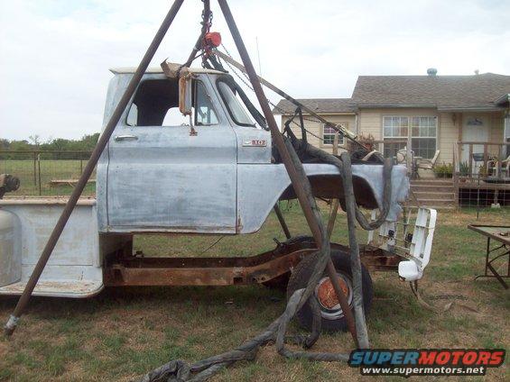 Unpainted truck cab and chassis suspended by a metal A-frame, with a single wheel visible