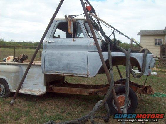 Side view of a light blue pickup truck cab lifted by a metal frame, showing its chassis and rear wheel