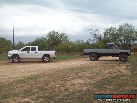 White Dodge Ram towing a lifted gray pickup truck with its hood up