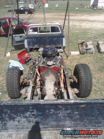 Pickup truck body lifted by a crane, engine and transmission removed, sitting on chassis with wheels