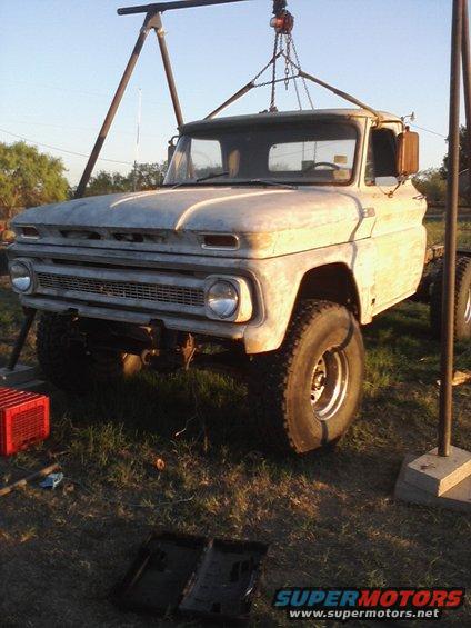 White pickup truck, lifted, with large tires, under a hoist. Grille and headlights visible