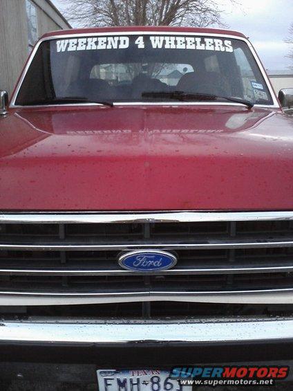 Red Ford Bronco front view, chrome grille with Ford emblem, 'WEEKEND 4 WHEELERS' sticker on windshield