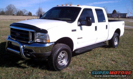 White 2002 Ford F-250 pickup truck with chrome bull bar and fender flares, parked on grass