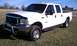 2002 Ford F-250 - A white 2002 Ford F-250 pickup truck is viewed from a three-quarter front angle, parked outdoors on a grassy field under a clear blue sky.