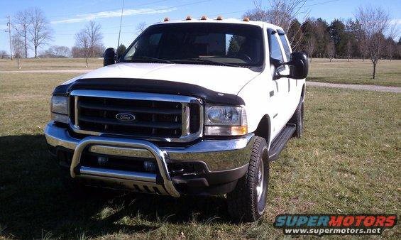 White 2002 Ford F-250 truck with chrome bull bar and fender flares, parked on grass