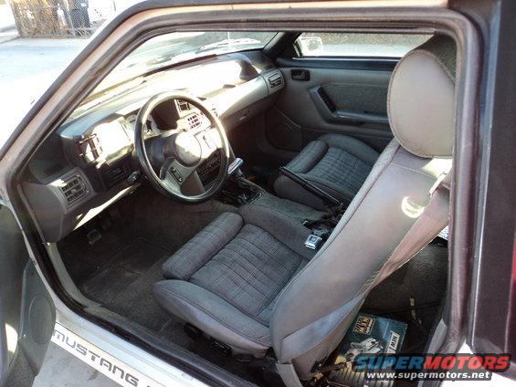 Gray fabric interior of a 1989 Ford Mustang, showing dashboard, steering wheel, and seats