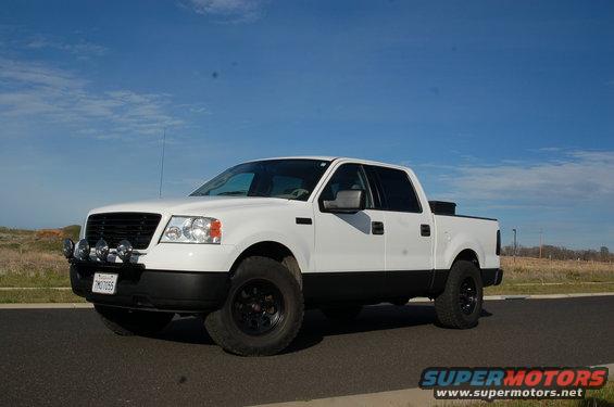 White Ford F-150 truck with black trim and aftermarket lights, viewed from the front three-quarter angle