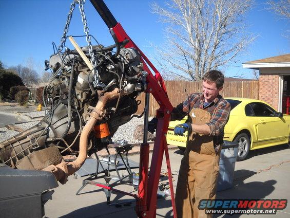 Guy using engine hoist to lift out a motor. Yellow Mustang in background