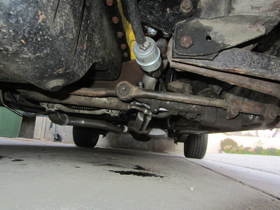 Underside view of a vehicle's suspension and exhaust system. Oil stains on the ground
